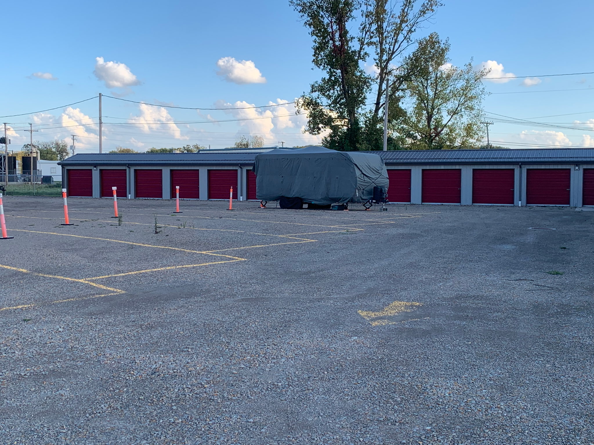 Row of red roll-up storage doors with numbered gravel parking spaces at Storage Source